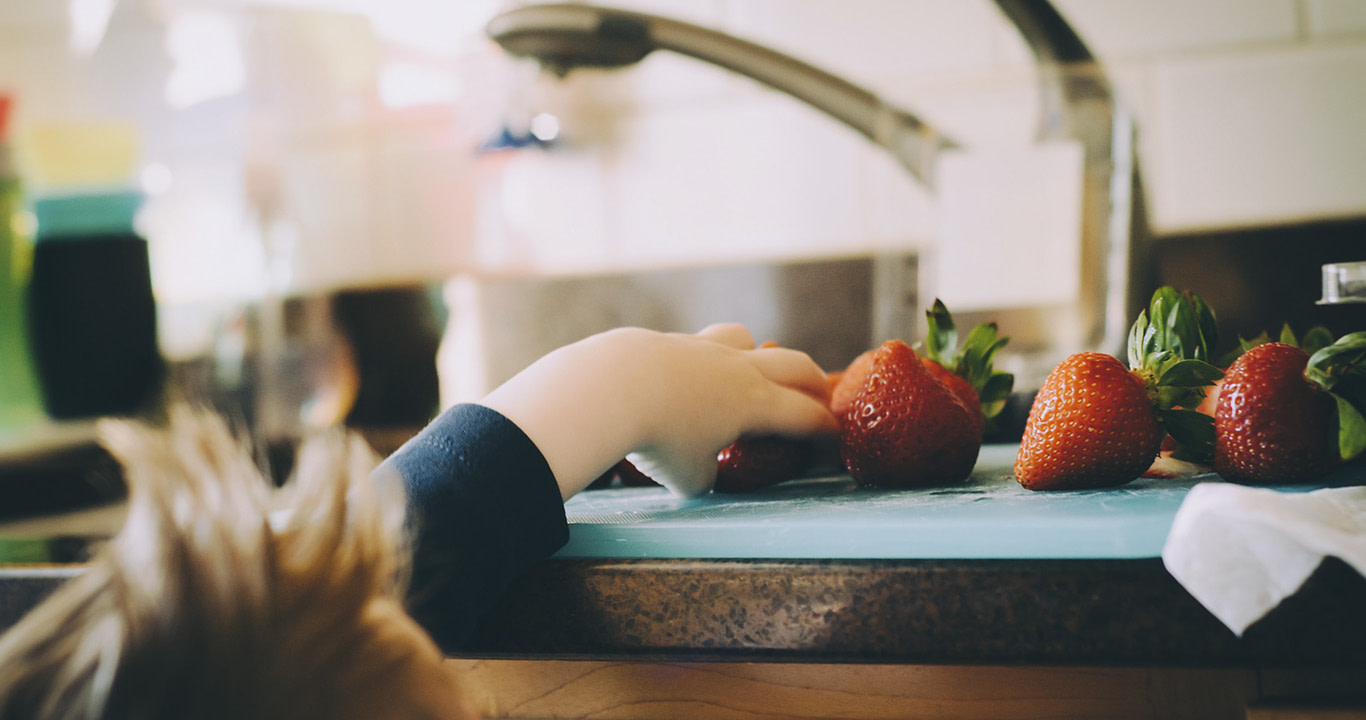 Niño merendando fresas Niño tomando una fresa de un mesón para merendar